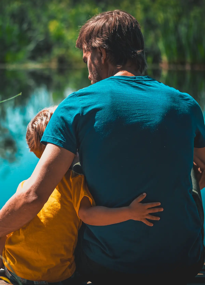 An adult and child sitting together by a lake